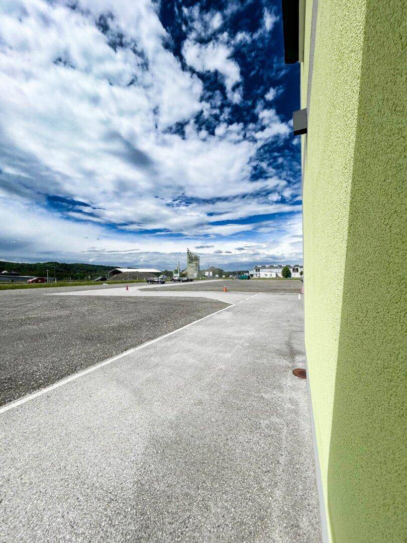 Blick entlang der Gebäudeseite auf eine gepflasterte Fläche mit weiter Sicht auf die Umgebung unter blauem Himmel.