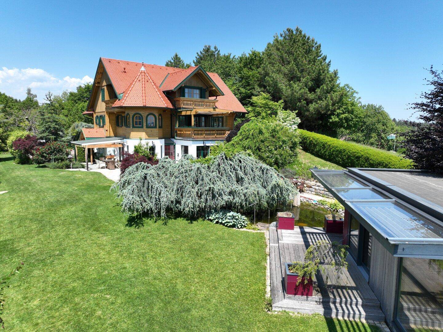 Luftaufnahme des Anwesens mit traditionellem Haus, großem Garten, Teich und modernem Nebengebäude.