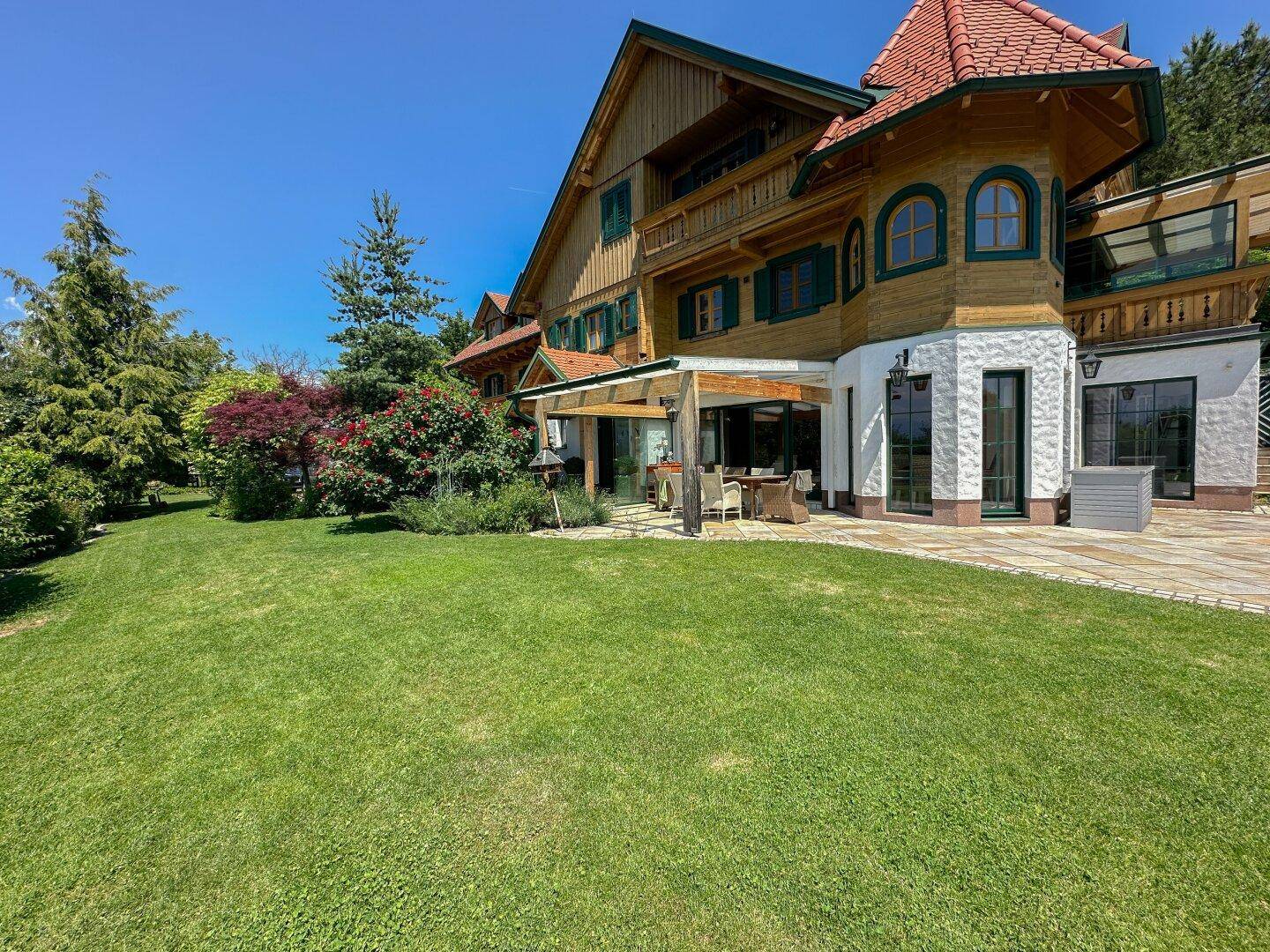 Großzügige Rasenfläche vor dem charmanten Holzhaus mit traditioneller Architektur und sonniger Terrasse.