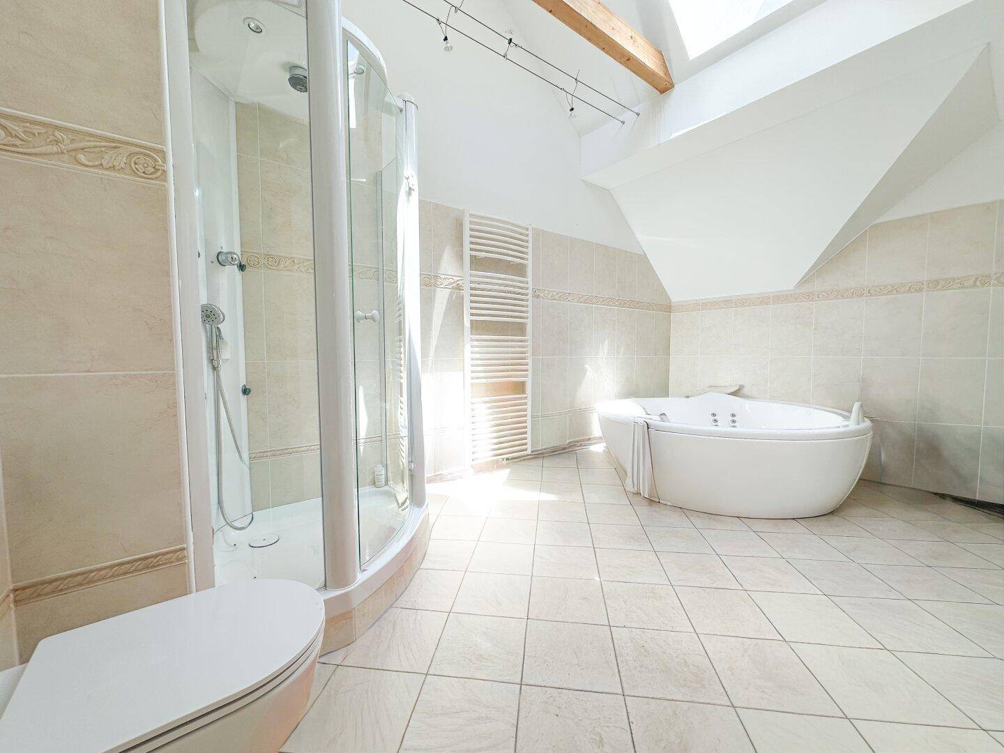 Helles Badezimmer mit Eckdusche, Toilette und großem Whirlpool unter einem Dachfenster.