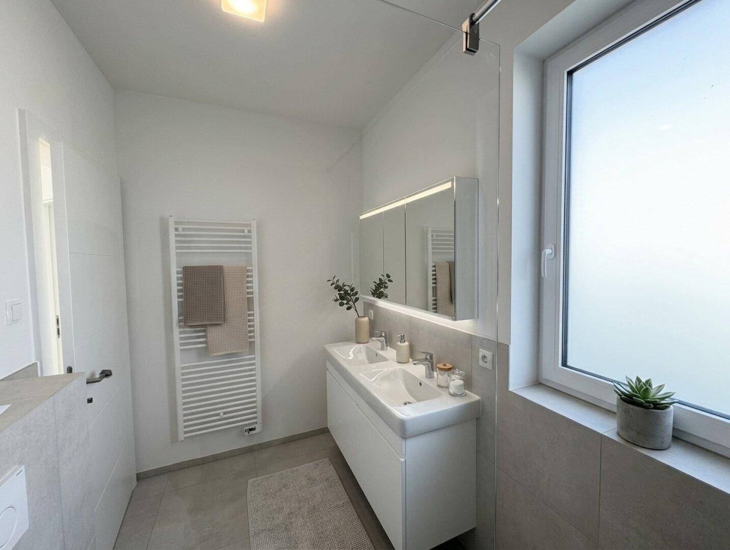 Helles Badezimmer mit Doppelwaschbecken, Spiegelschrank und beheiztem Handtuchhalter.