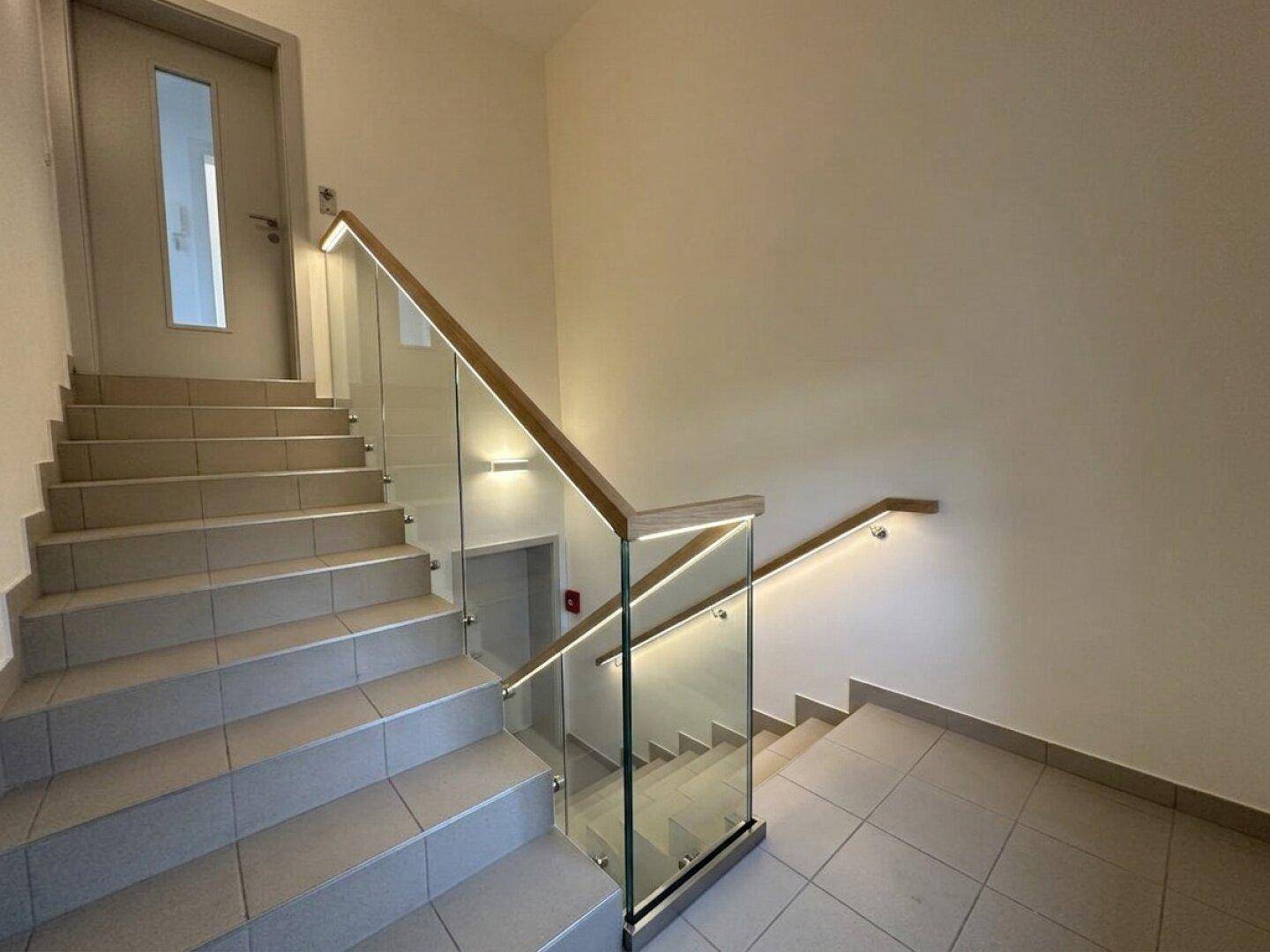 Modernes Treppenhaus mit Glasgeländer, Holzhandlauf und integrierter Beleuchtung.