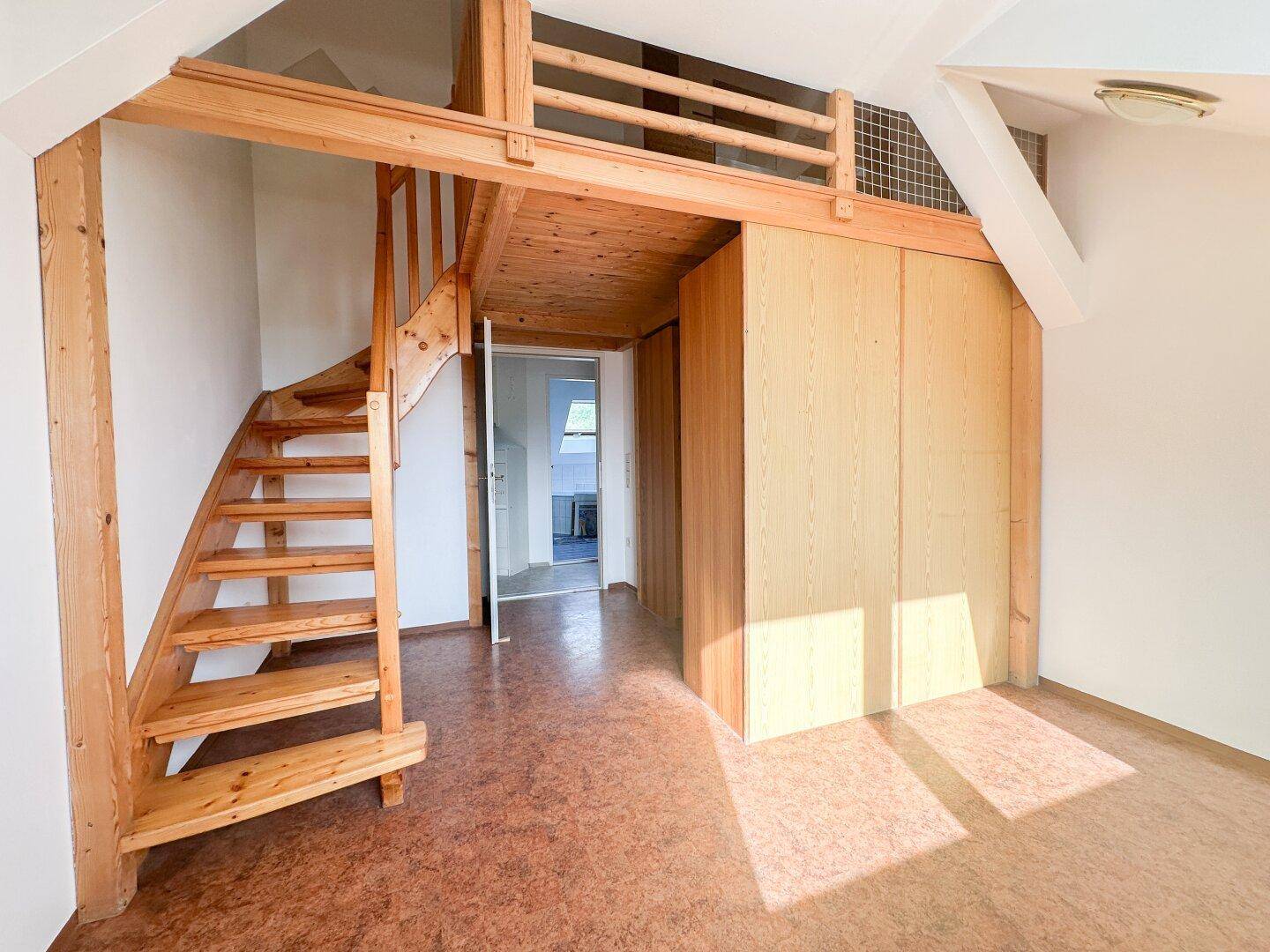 Geräumiges Zimmer mit Holztreppe, Dachschrägen und Korkboden, ideal als Arbeits- oder Wohnbereich.