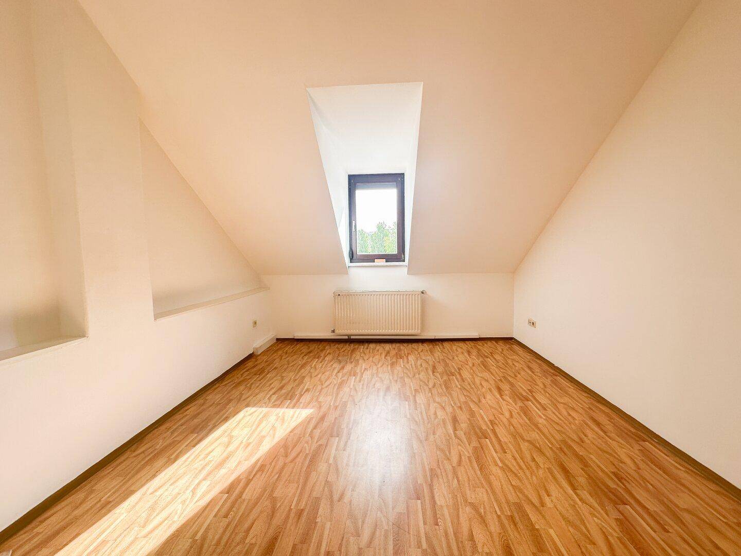 Leeres Schlafzimmer im Dachgeschoss mit Dachschrägen, Holzboden und Dachfenster.