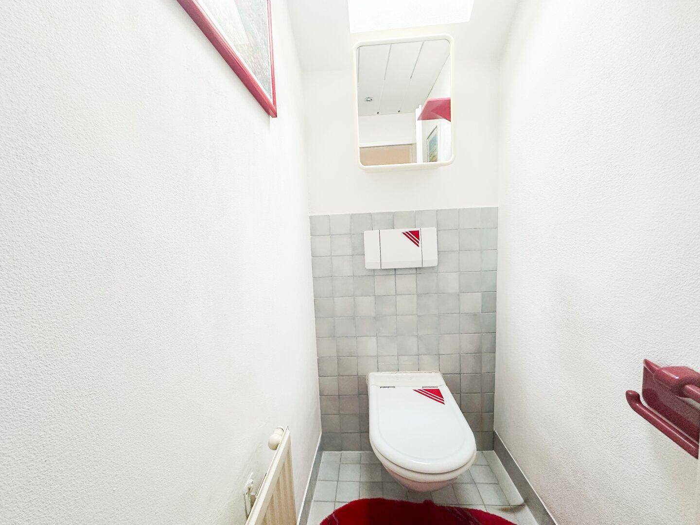 Einfaches Gäste-WC mit Toilette, kleinem Waschbecken und Fliesen an der Wand.