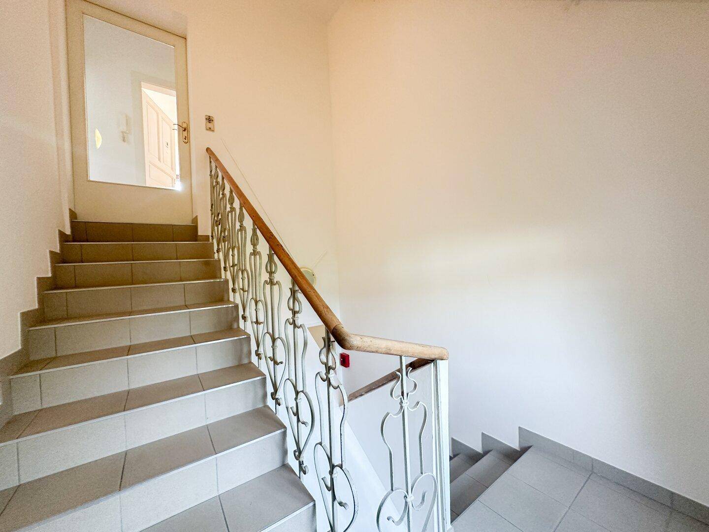 Treppenhaus mit schmiedeeisernem Geländer und Fliesenboden in einem älteren Gebäude.