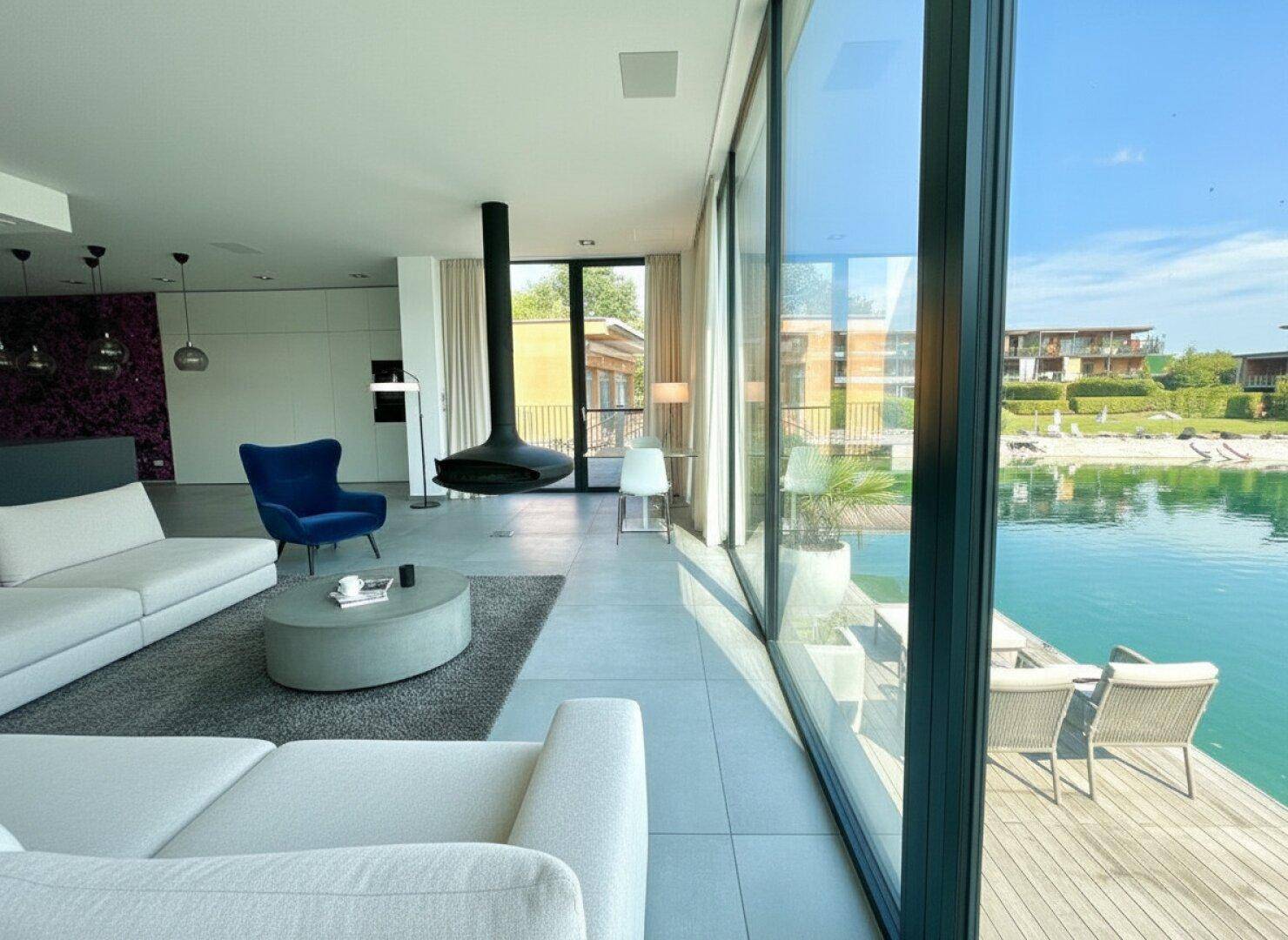 Helles Wohnzimmer mit raumhohen Fenstern, Seeblick und modernem Hängekamin.