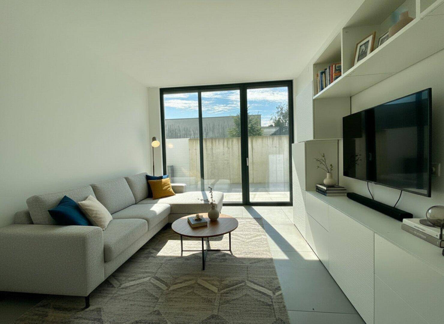 Helles Wohnzimmer mit Sofa, Fernseher und Zugang zu einem Außenbereich.