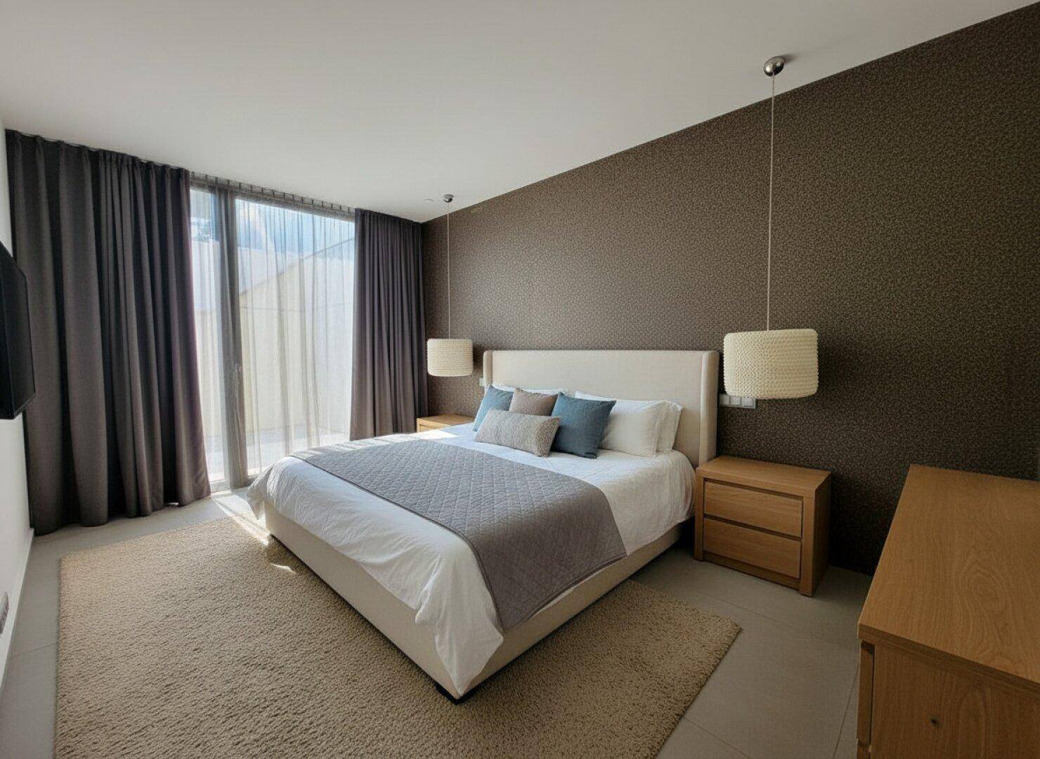 Gemütliches Schlafzimmer mit großen Fenstern, Vorhängen und Holzelementen.