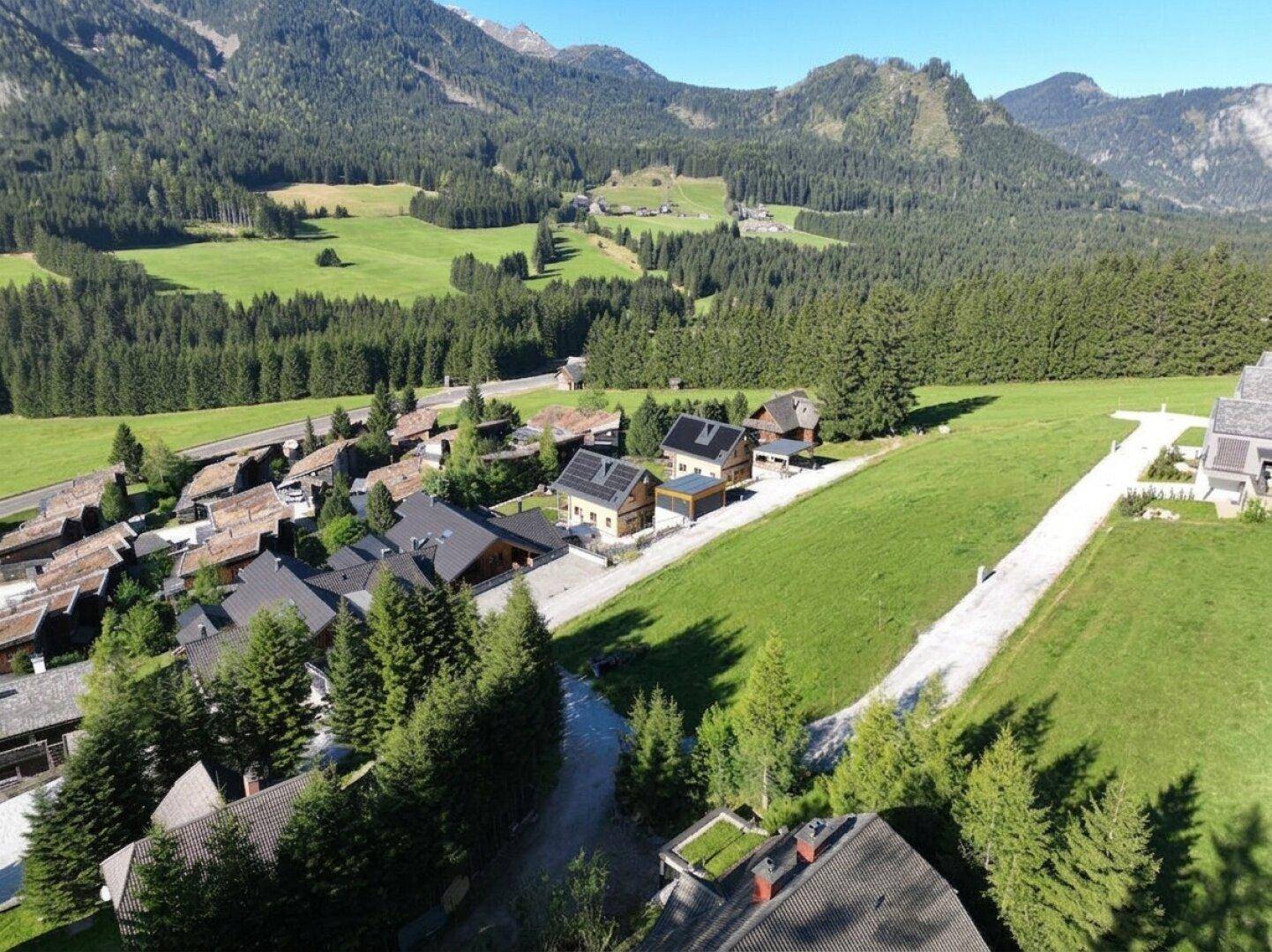Weitläufige Luftaufnahme einer alpinen Landschaft mit Wäldern, Wiesen und verstreuten Siedlungen.