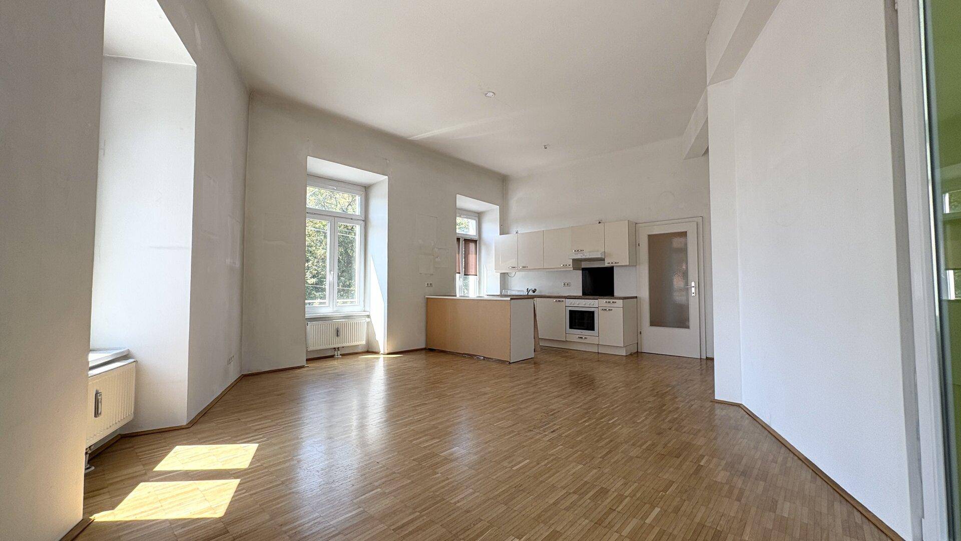 Offener Wohnbereich mit integrierter Küche, Parkettboden und viel natürlichem Licht durch die Fenster.