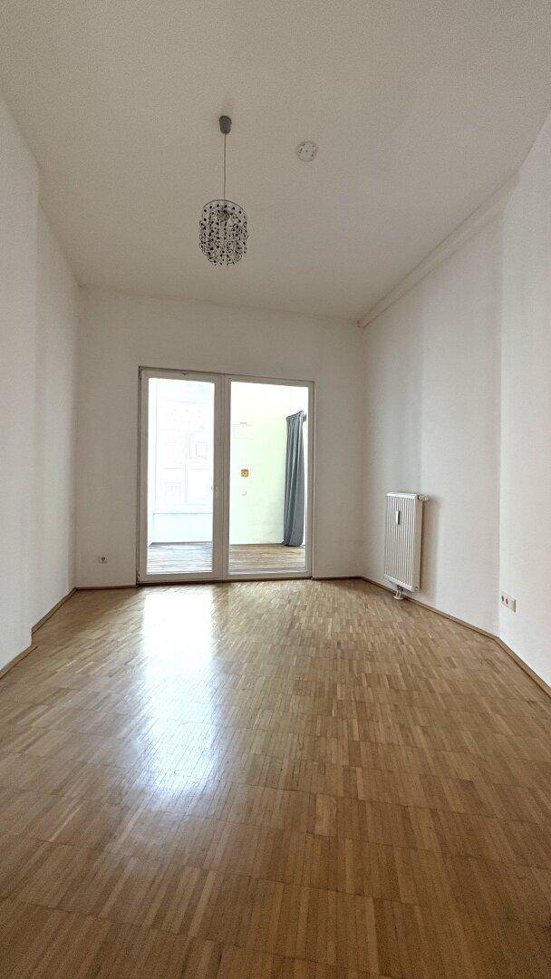 Leerer Wohnraum mit Parkettboden und einer modernen Deckenleuchte, die den Raum erhellt.