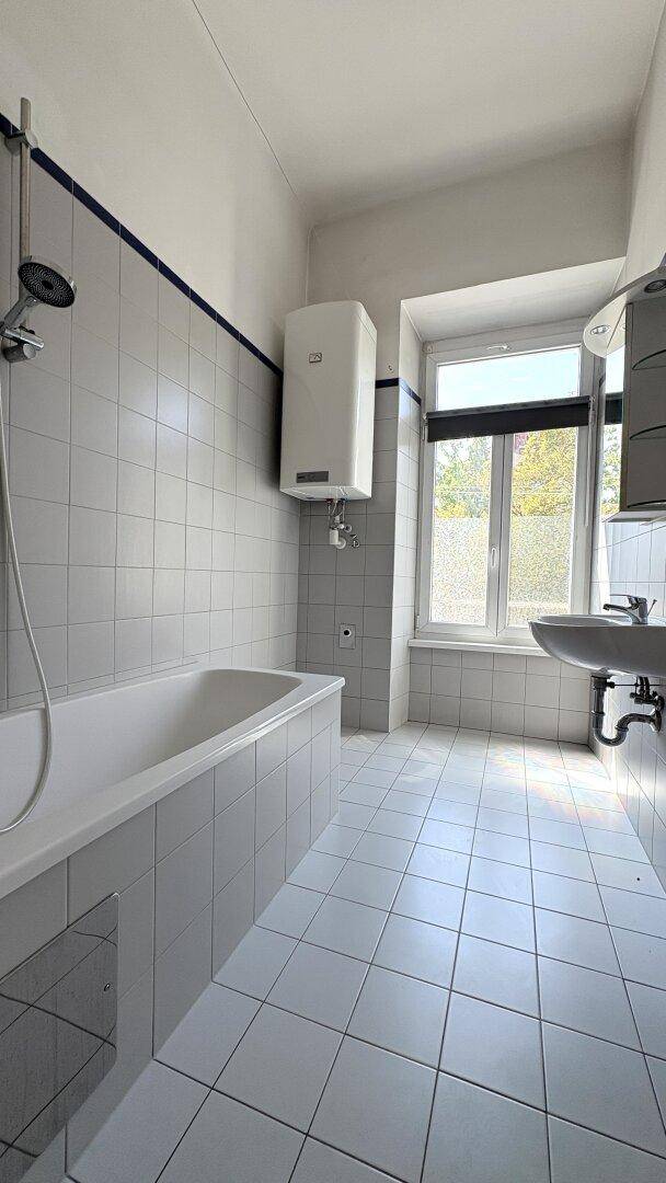Badezimmer mit Badewanne, Dusche und Fliesenboden, ausgestattet mit einem Fenster für Tageslicht.