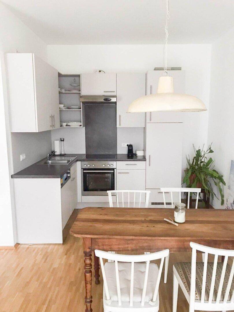Moderne weiße Küche mit Holztisch und Stühlen, integriert in einen offenen Wohnbereich.