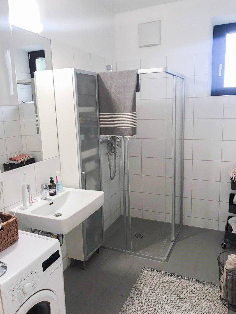 Modernes Badezimmer mit Dusche, Waschbecken und Waschmaschine, hell gefliest.