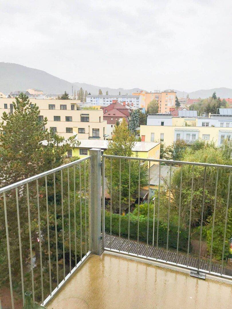 Balkon mit Blick auf die umliegende Wohnbebauung und grüne Hügel im Hintergrund.