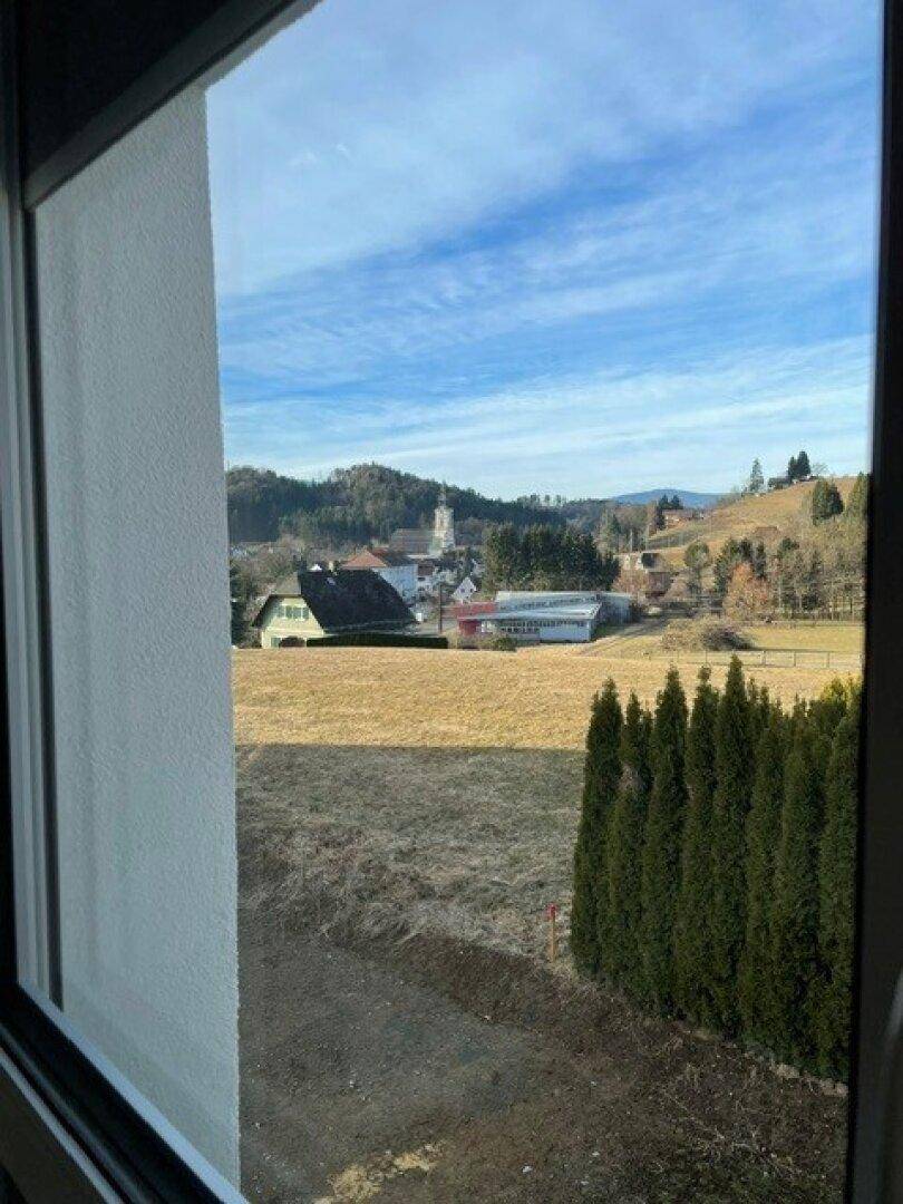 Weitblick aus dem Fenster über eine ländliche Landschaft mit Feldern, Bäumen und einem Dorf mit Kirche.