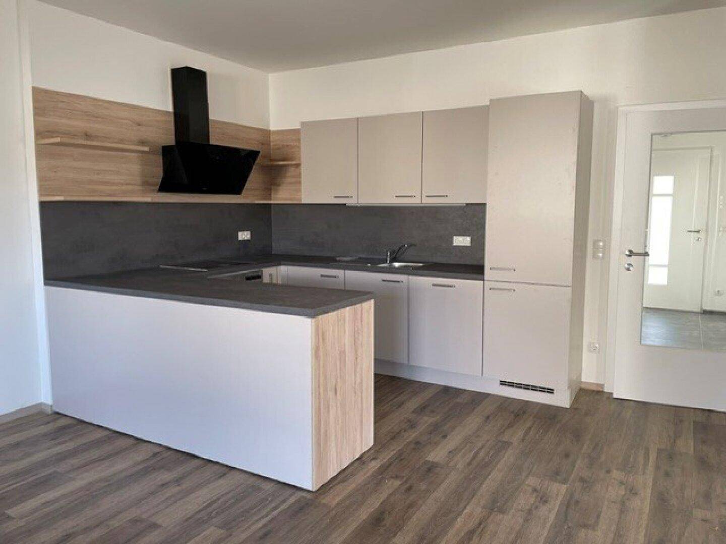 Moderne Einbauküche mit hellgrauen Fronten, dunkler Arbeitsplatte und Holzdetails, offen zum Wohnbereich.