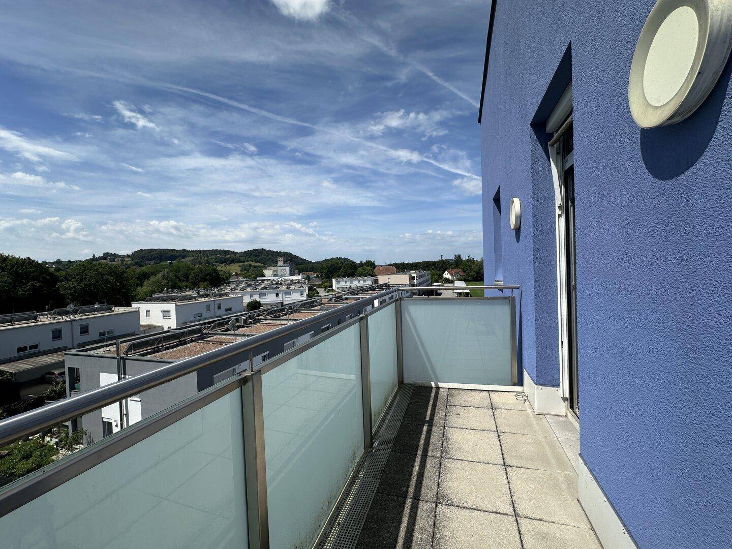 Balkon mit Fliesenboden, Glasgeländer und weitem Blick über die umliegende Landschaft.