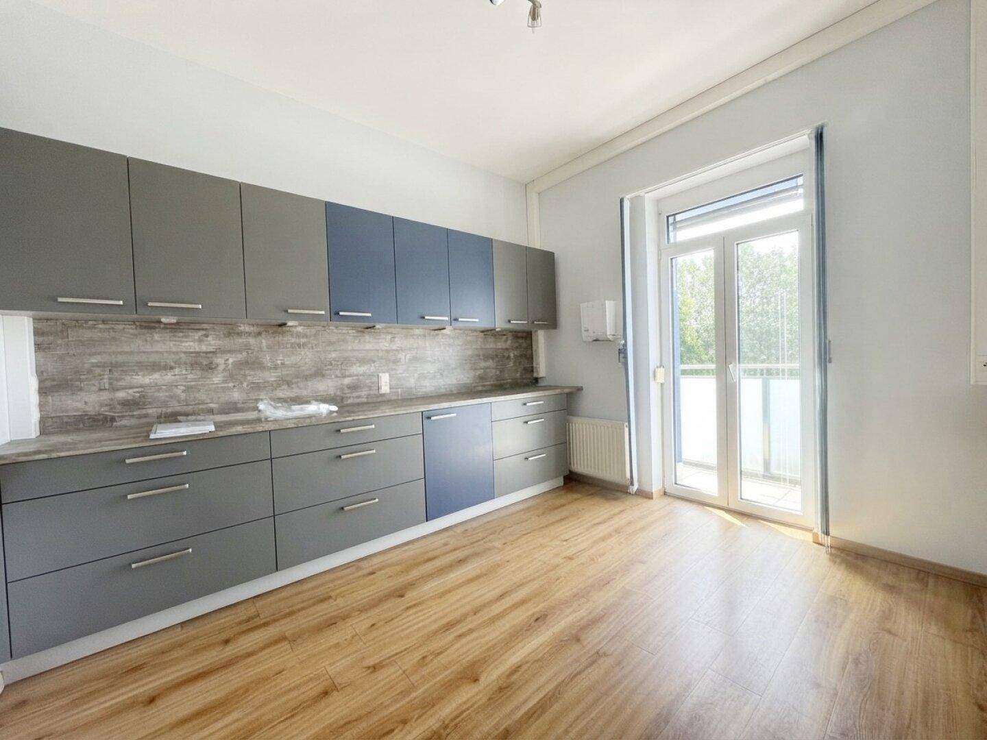 Moderne Küchenzeile mit grauen und blauen Schränken, Holzboden und Zugang zu einem Balkon.
