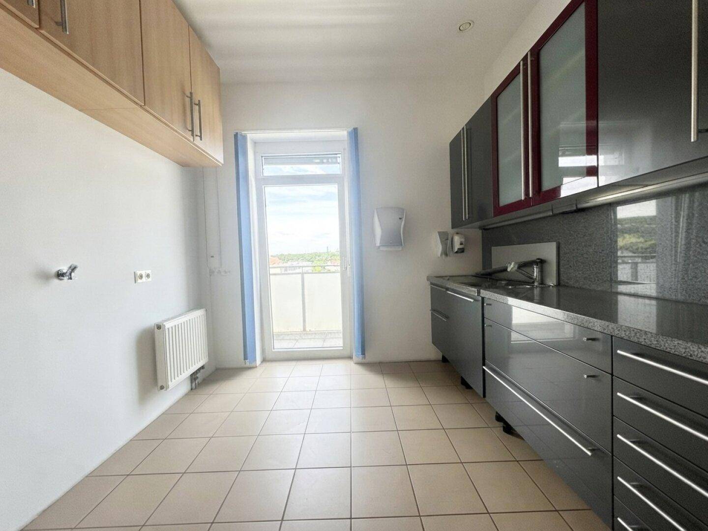 Funktionale Küchenzeile mit dunklen Schränken, Fliesenboden und Zugang zu einem Balkon.