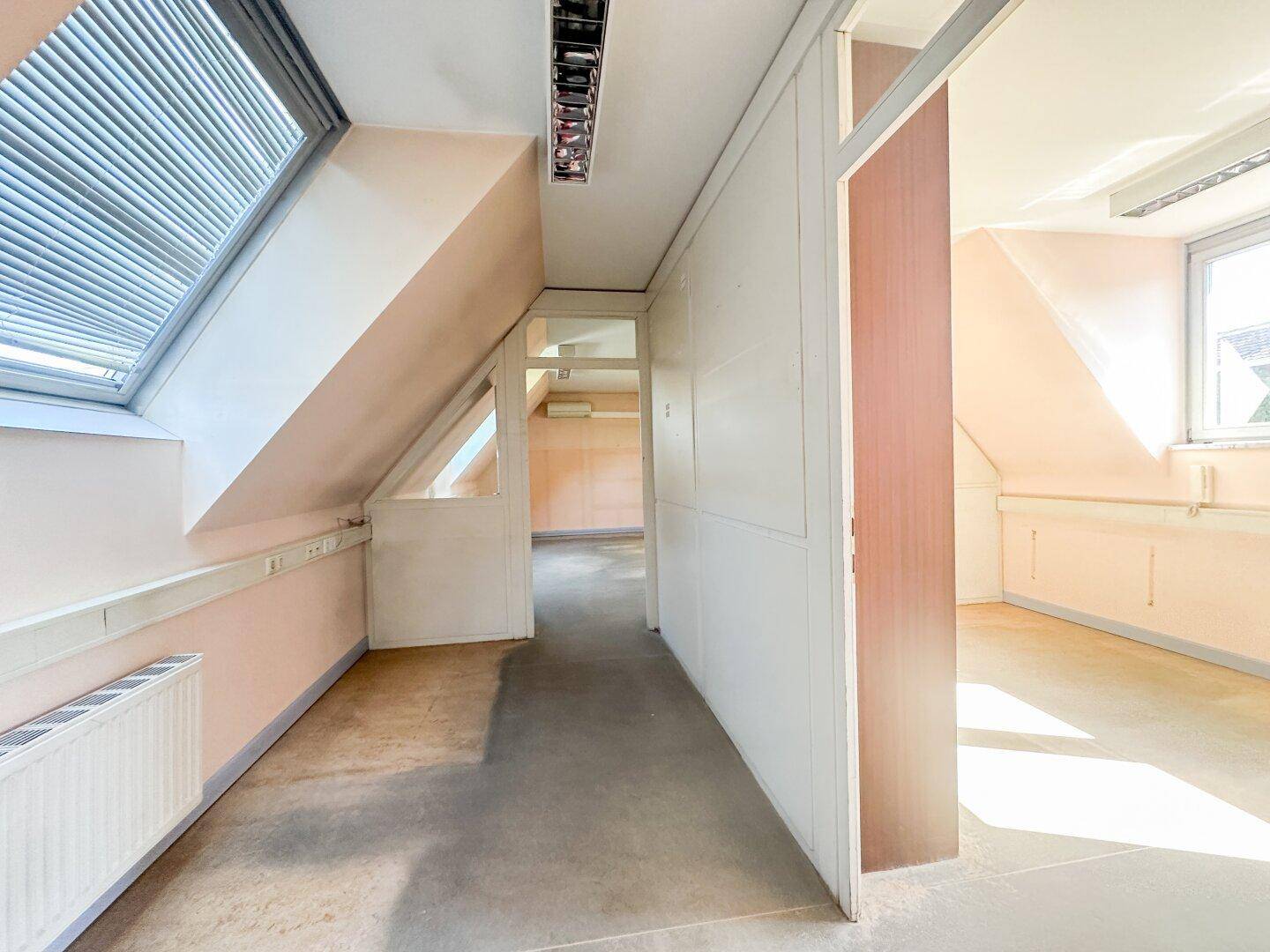 Ein leerer Dachgeschossraum mit Schrägen, einem Dachfenster und einem normalen Fenster, bereit zur Einrichtung.