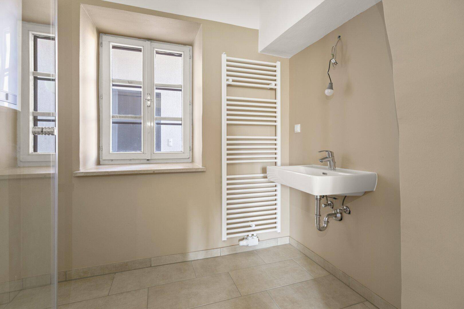 Modernes Badezimmer mit Waschbecken, Handtuchheizkörper und Fenster.
