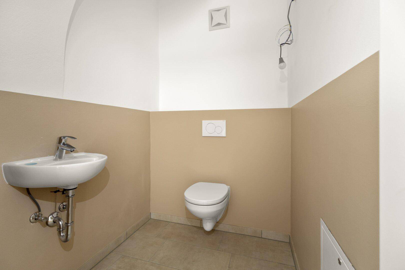 Separate Toilette mit wandhängendem WC, Waschbecken und Fliesenboden.