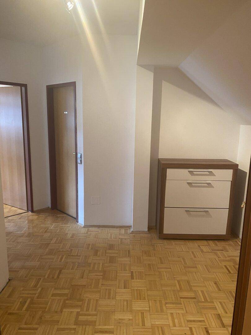 Heller Flurbereich mit Parkettboden, Dachschräge und einer Kommode, die zu den Zimmern führt.