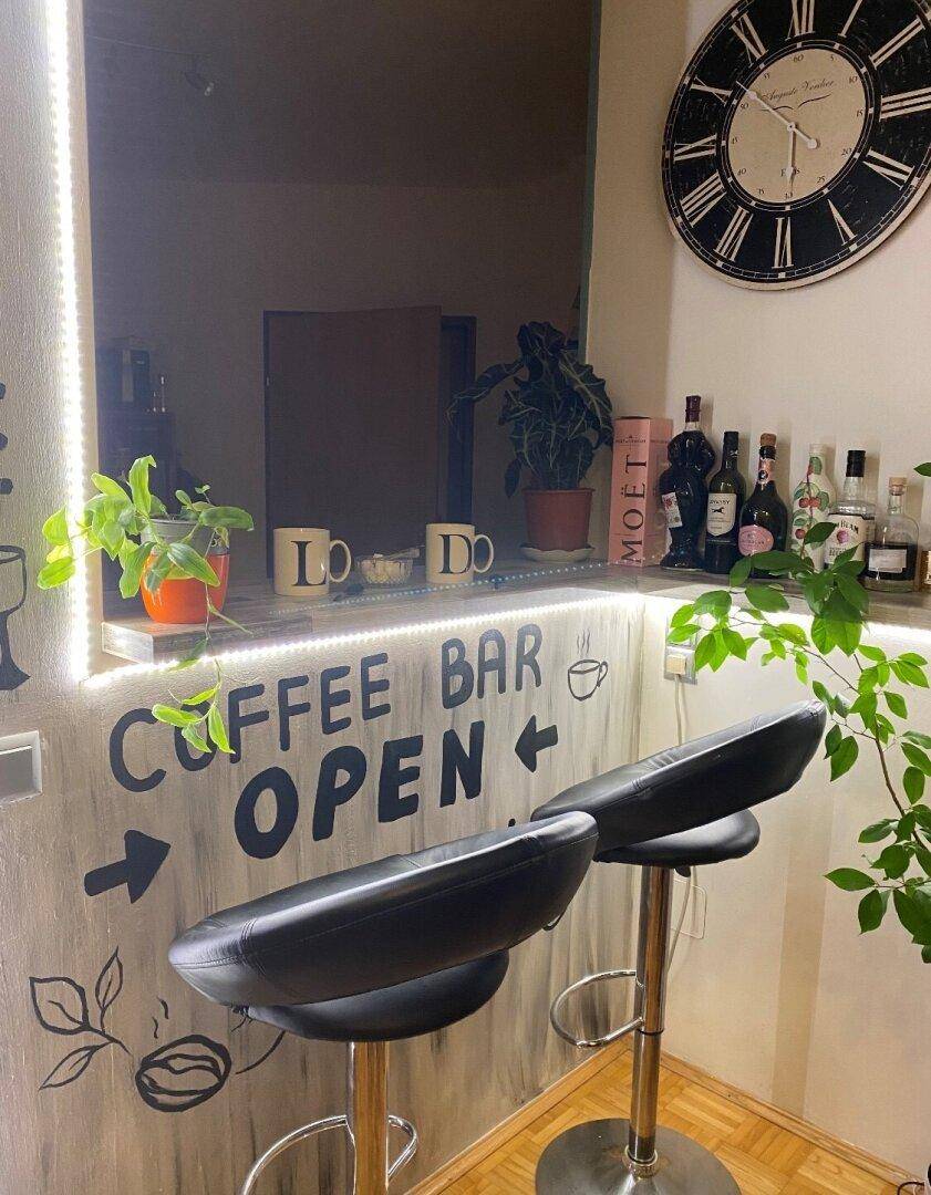 Gemütliche Kaffeebar mit Barhockern, Pflanzen und einer großen Wanduhr in einem Innenraum.