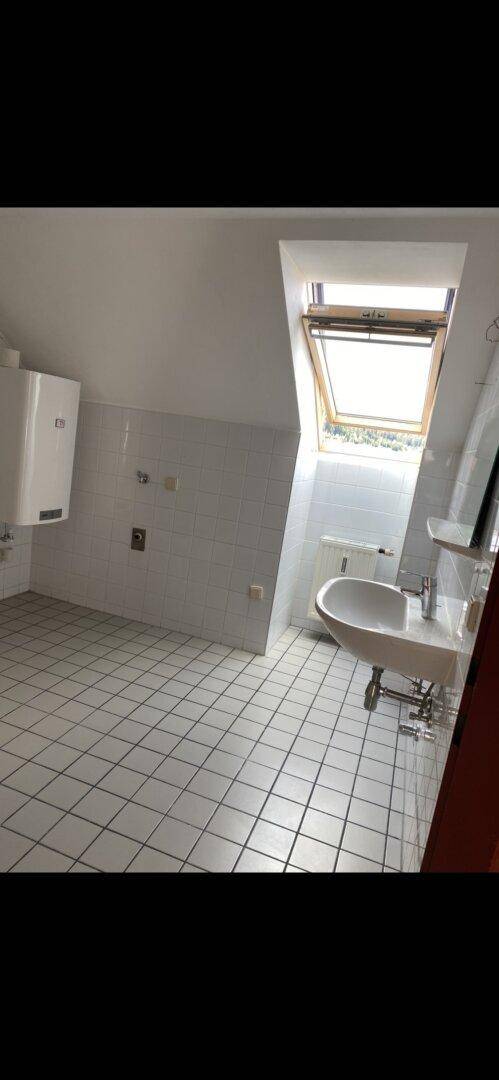 Helles Badezimmer mit Waschbecken, weißen Fliesen und einem Dachfenster für natürliches Licht.