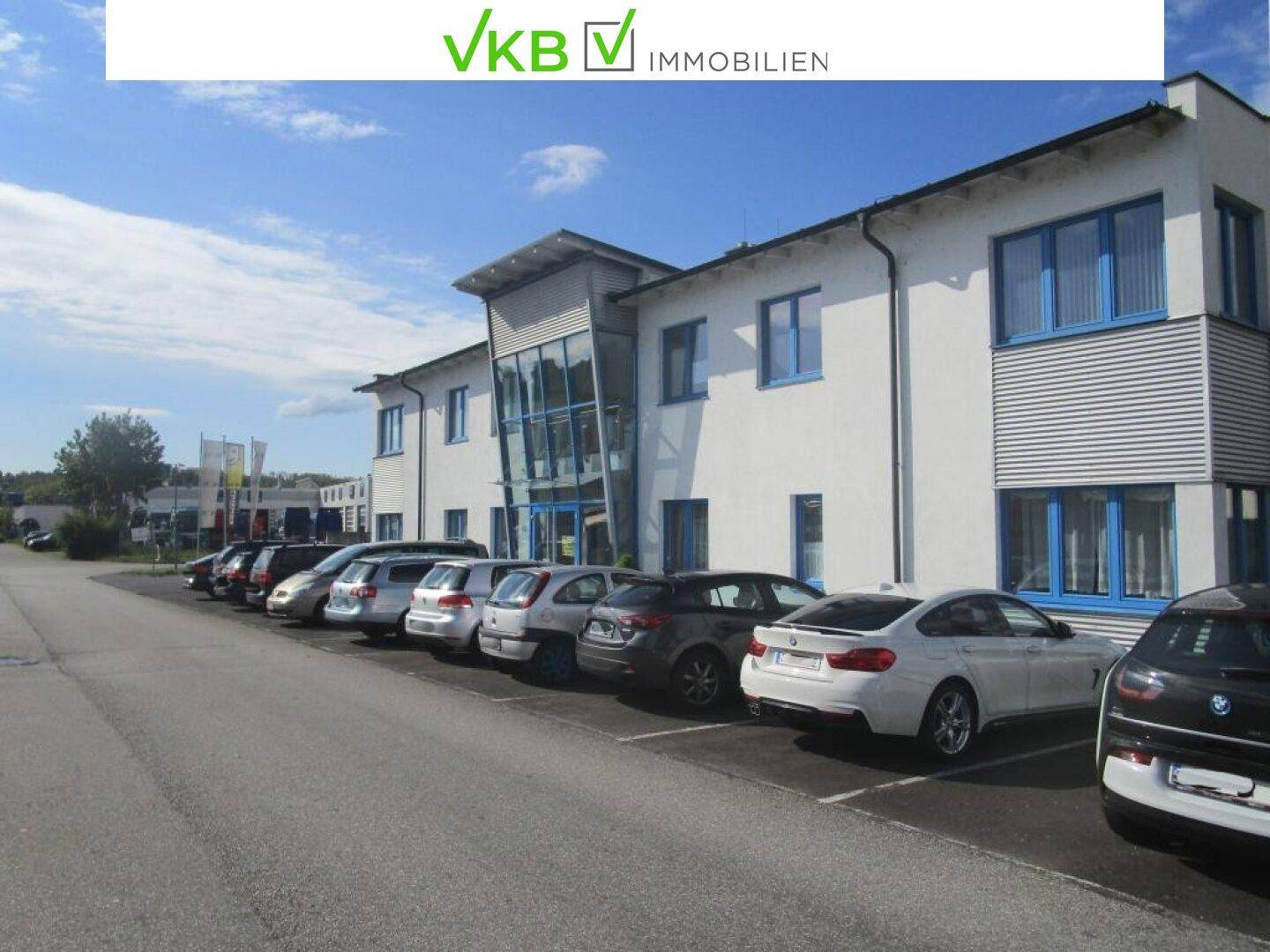 Modernes Geschäftsgebäude mit vielen Parkplätzen unter blauem Himmel, ideal für Unternehmen.