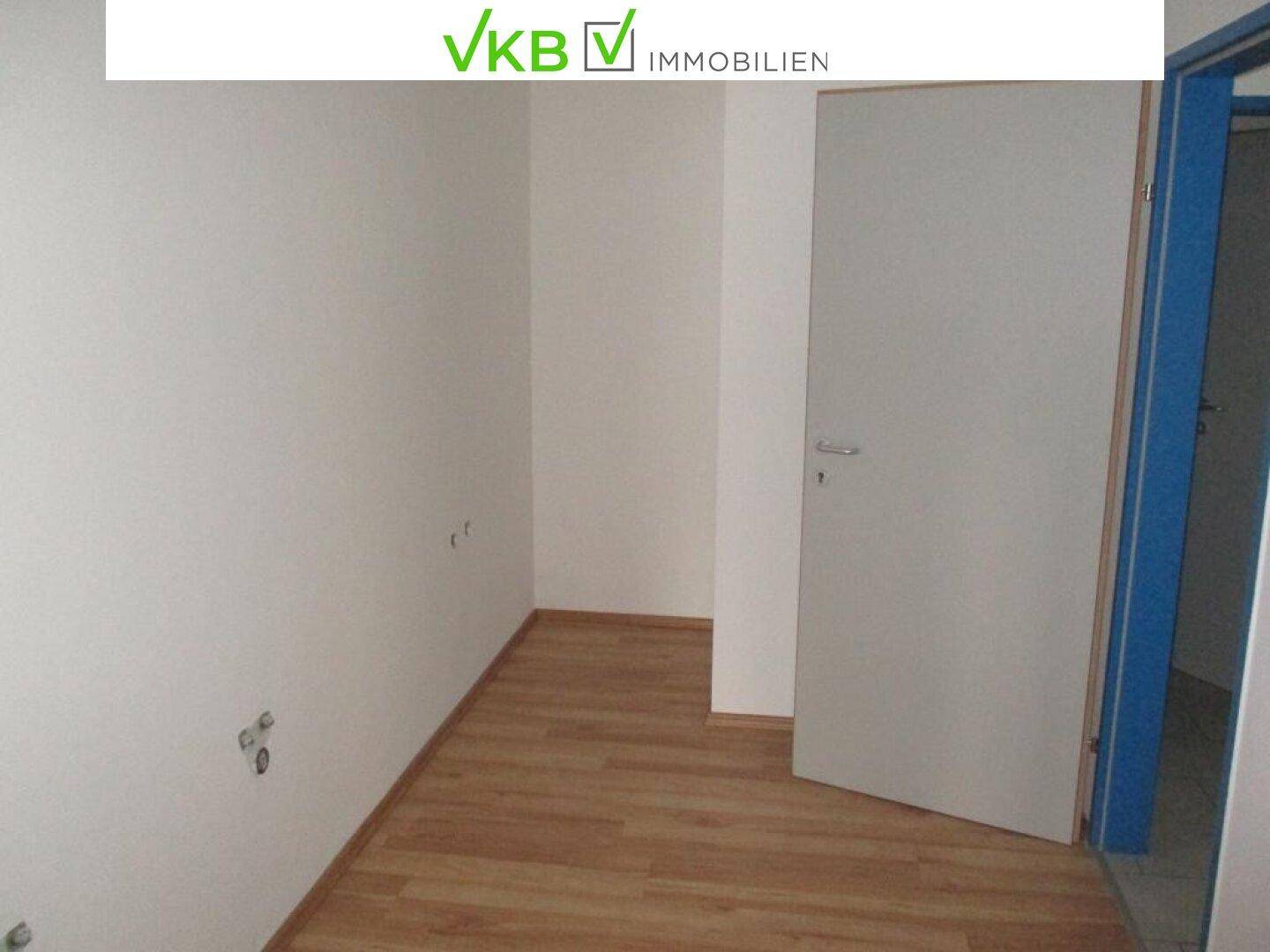 Leerer Raum mit Laminatboden und offener Tür, bereit für neue Nutzung oder Einrichtung.