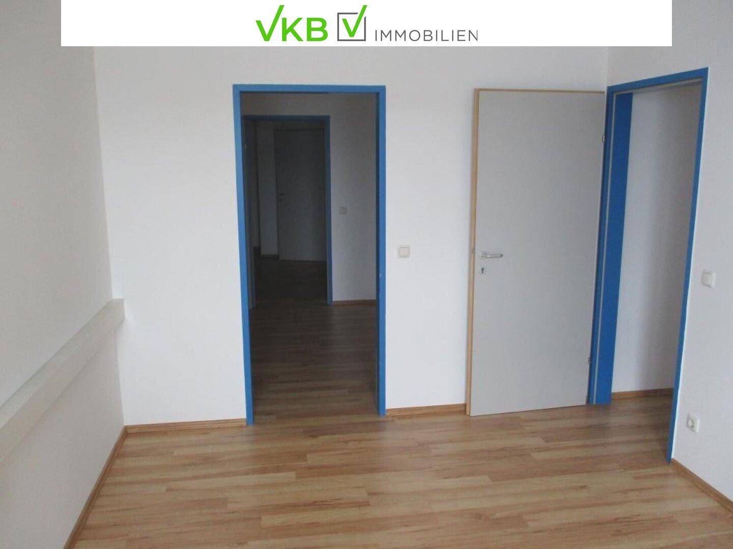 Leerer Raum mit Laminatboden und zwei offenen Türen, die zu weiteren Bereichen führen.