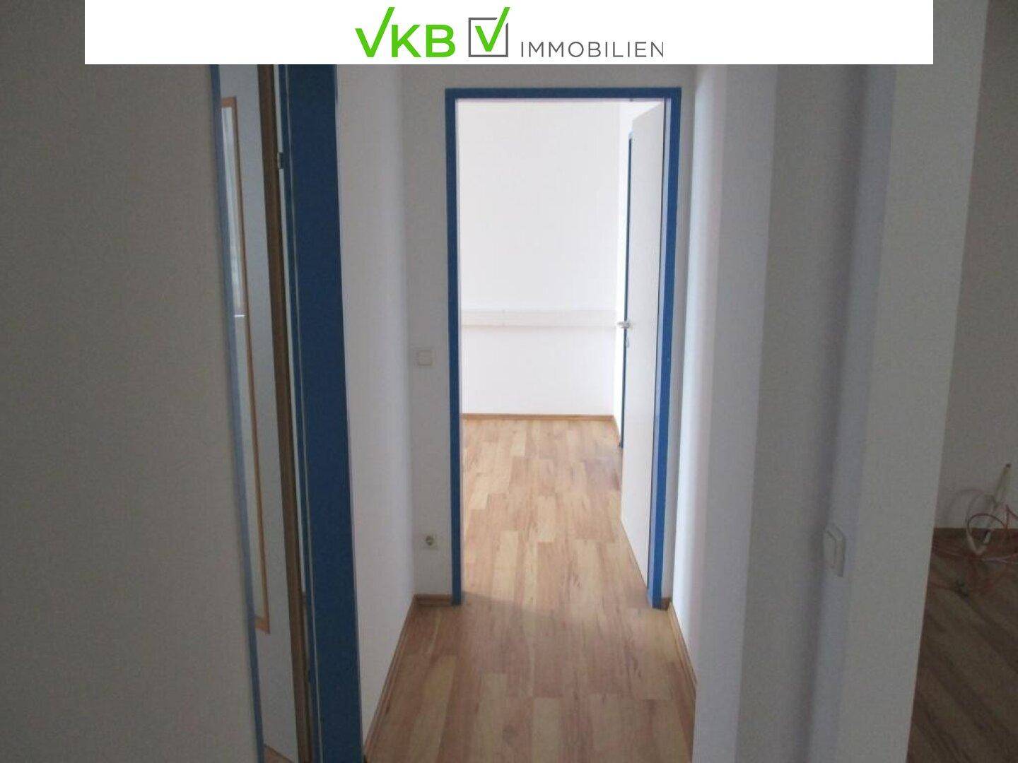 Langer, heller Flur mit Laminatboden und blauen Türrahmen, der zu mehreren Zimmern führt.