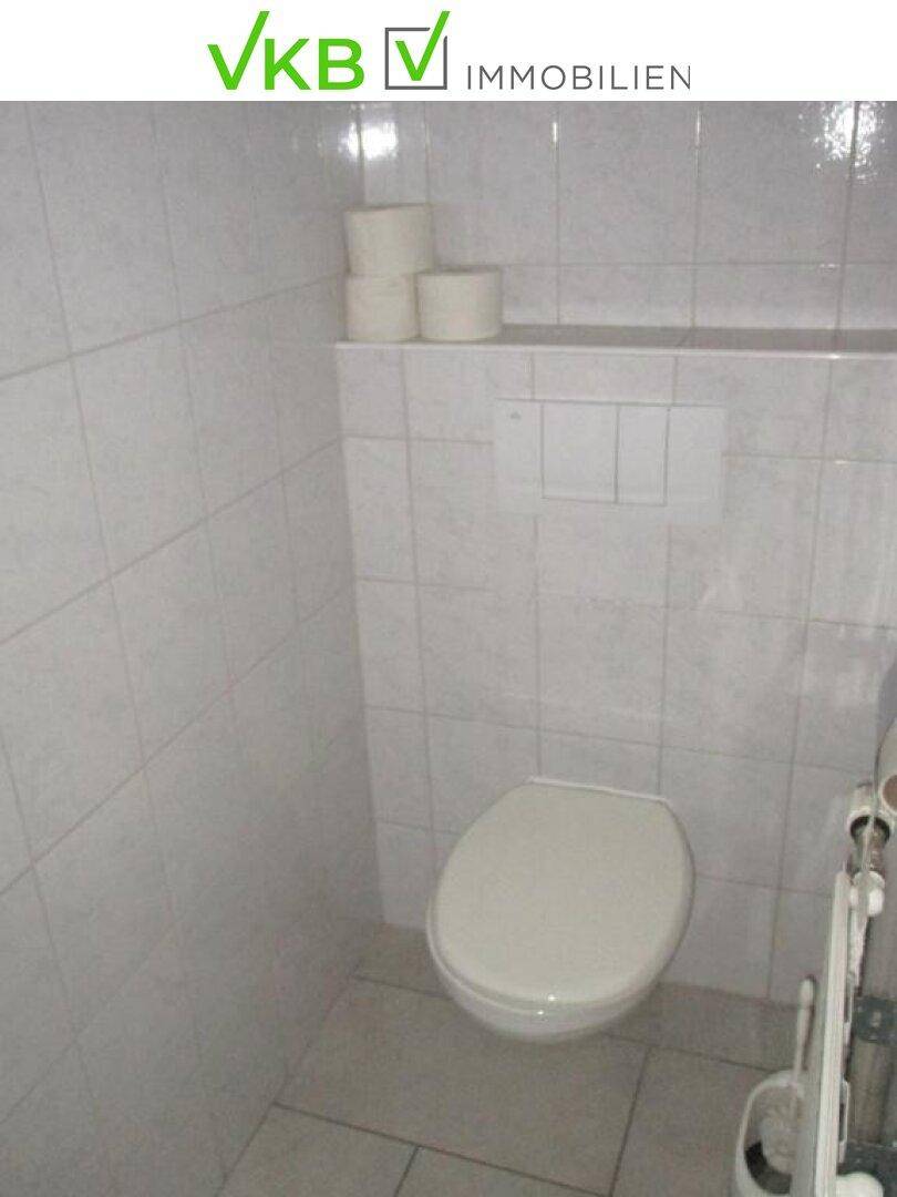 Kleiner Toilettenraum mit weißen Fliesen an Wänden und Boden sowie einer Wandtoilette.