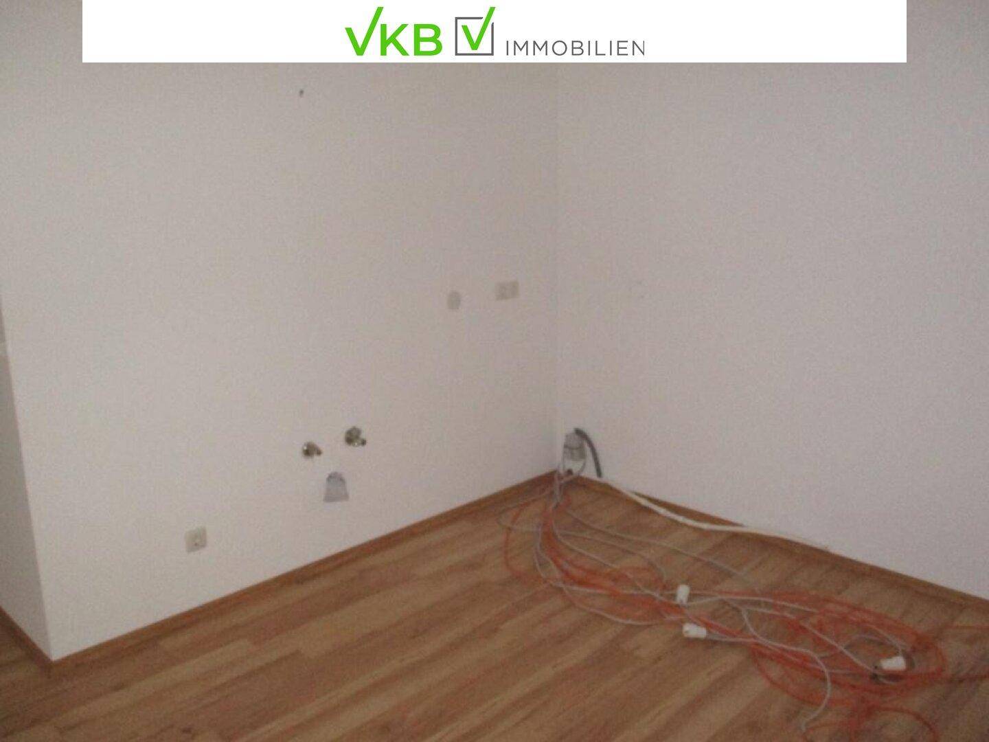 Ecke eines Büroraums mit Laminatboden und sichtbaren Kabelanschlüssen an der Wand.