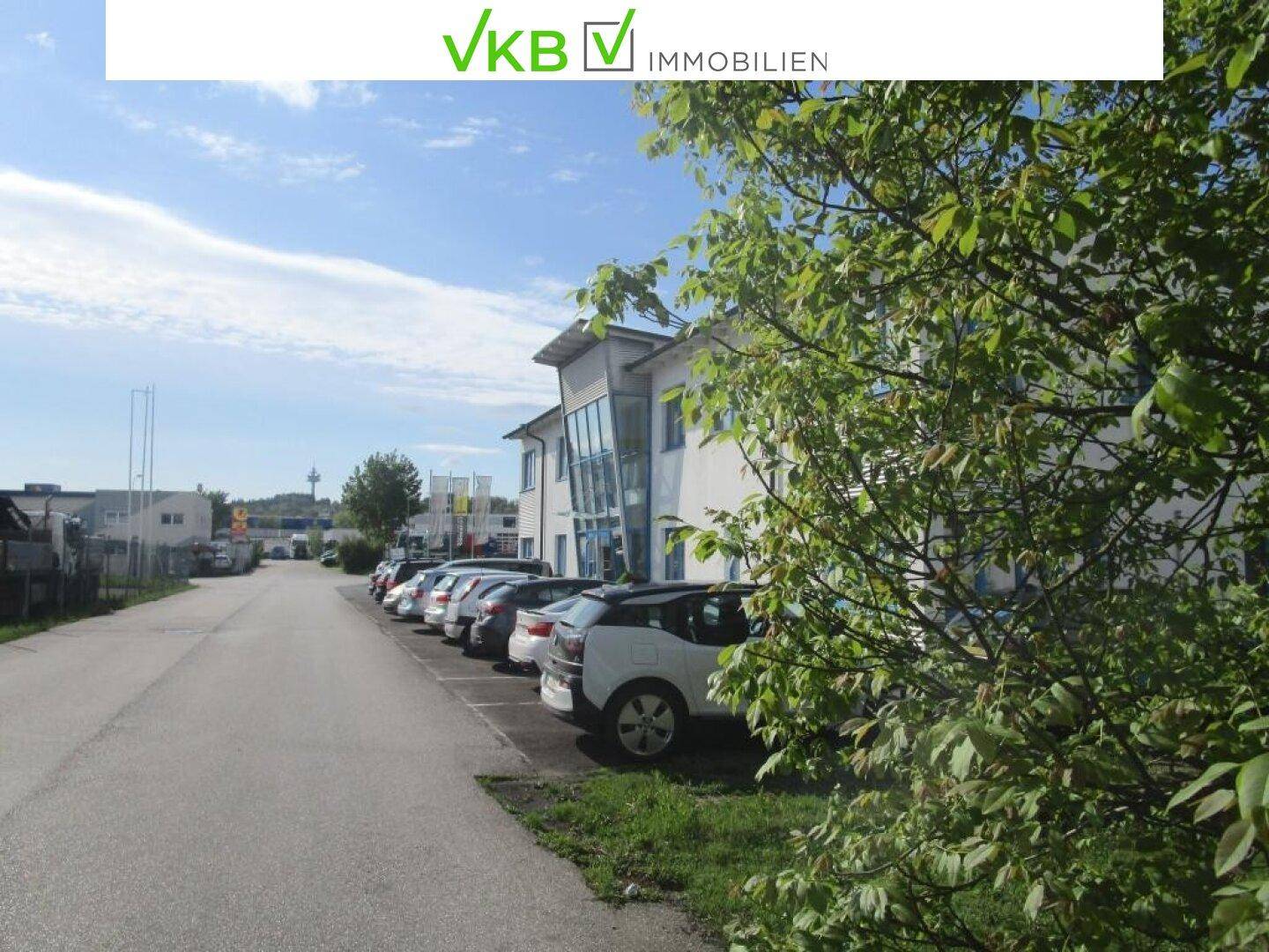 Außenansicht eines Gewerbegebäudes mit Parkplätzen und Bäumen im Vordergrund.