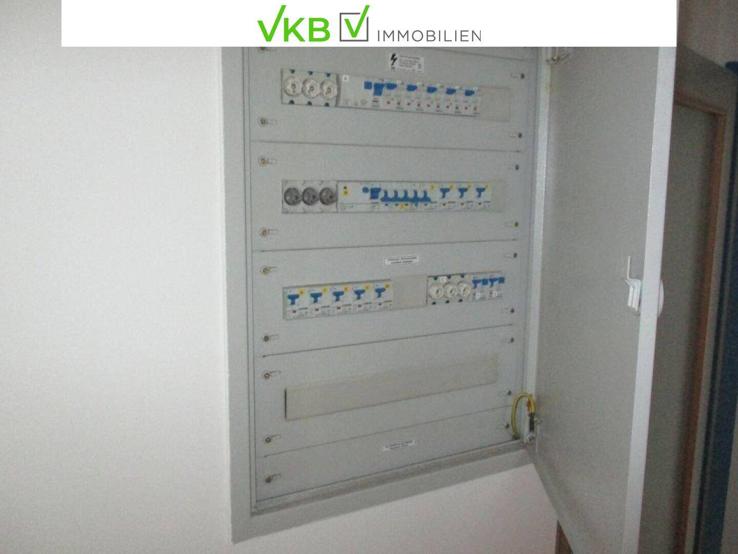 Offener Sicherungskasten mit vielen Schaltern und Verkabelungen an einer weißen Wand.