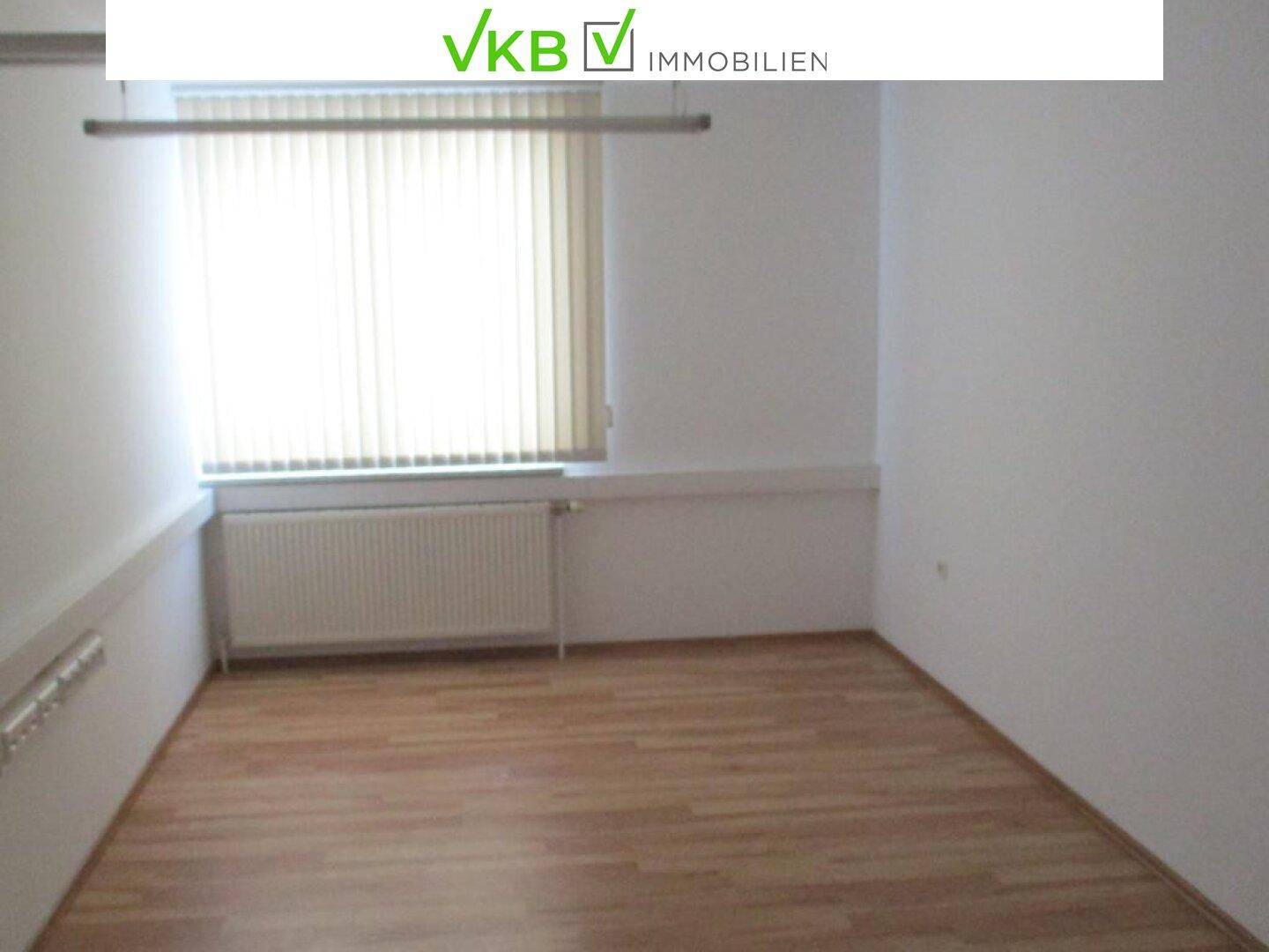 Kleineres Büro mit Laminatboden, einem Fenster mit Jalousie und einem Heizkörper darunter.