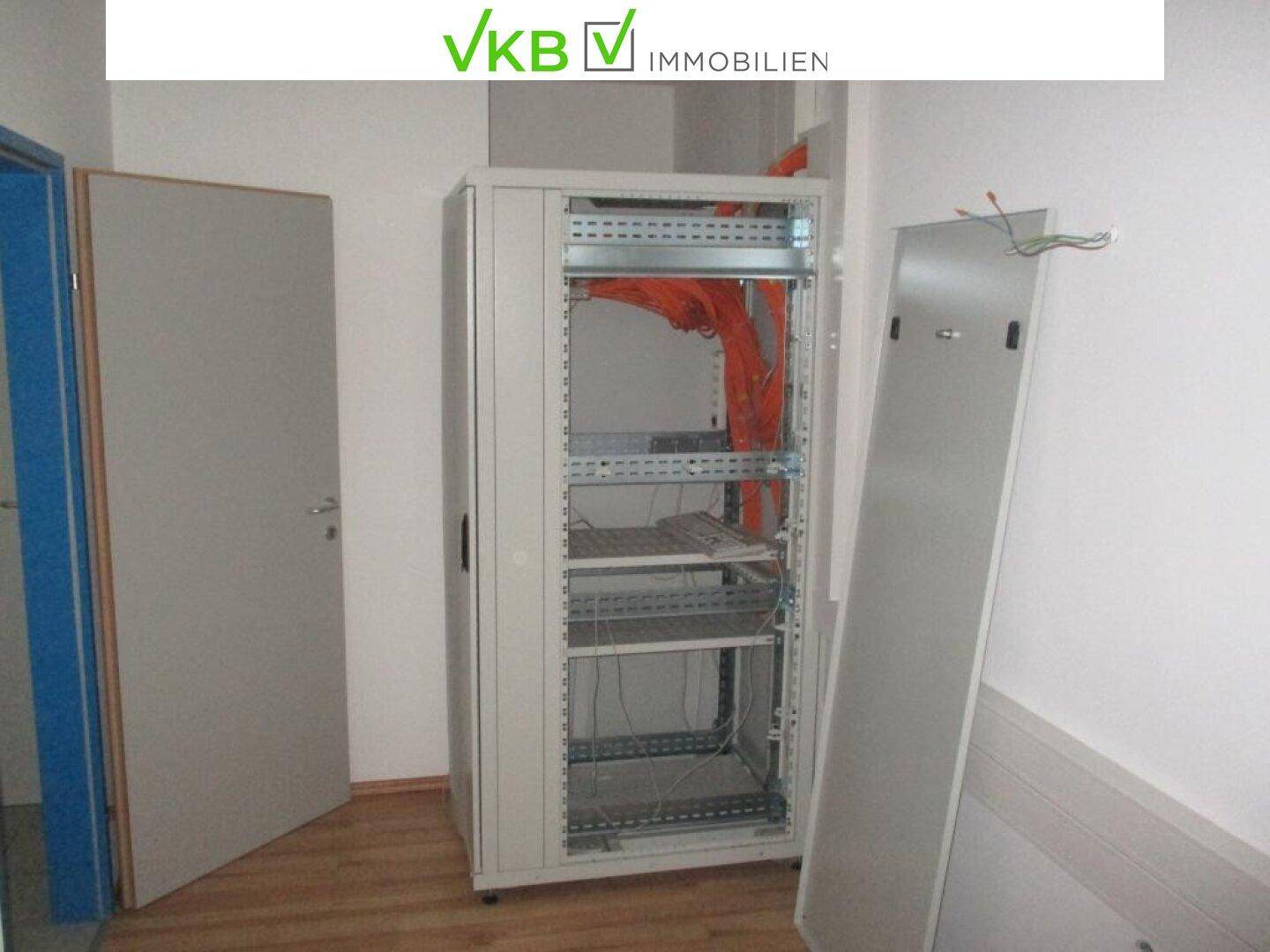 Serverschrank in einem Raum mit Holzboden und sichtbaren orangefarbenen Kabeln.