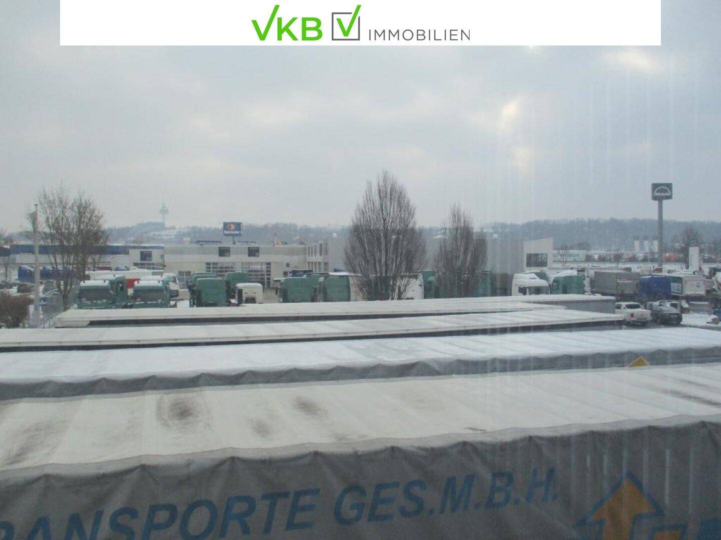Blick aus dem Fenster auf ein Gewerbegebiet mit Lastwagen und Gebäuden unter bewölktem Himmel.