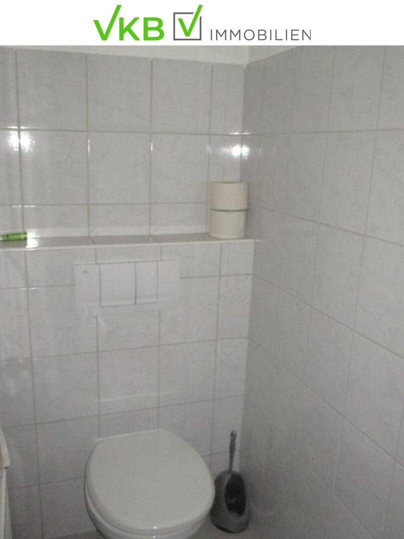 Kleines Badezimmer mit weiß gefliesten Wänden und einer Toilette, sauber und funktional.