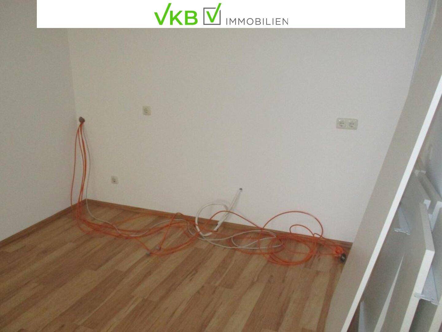 Ecke eines Büroraums mit Laminatboden und sichtbaren Kabeln an der Wand.