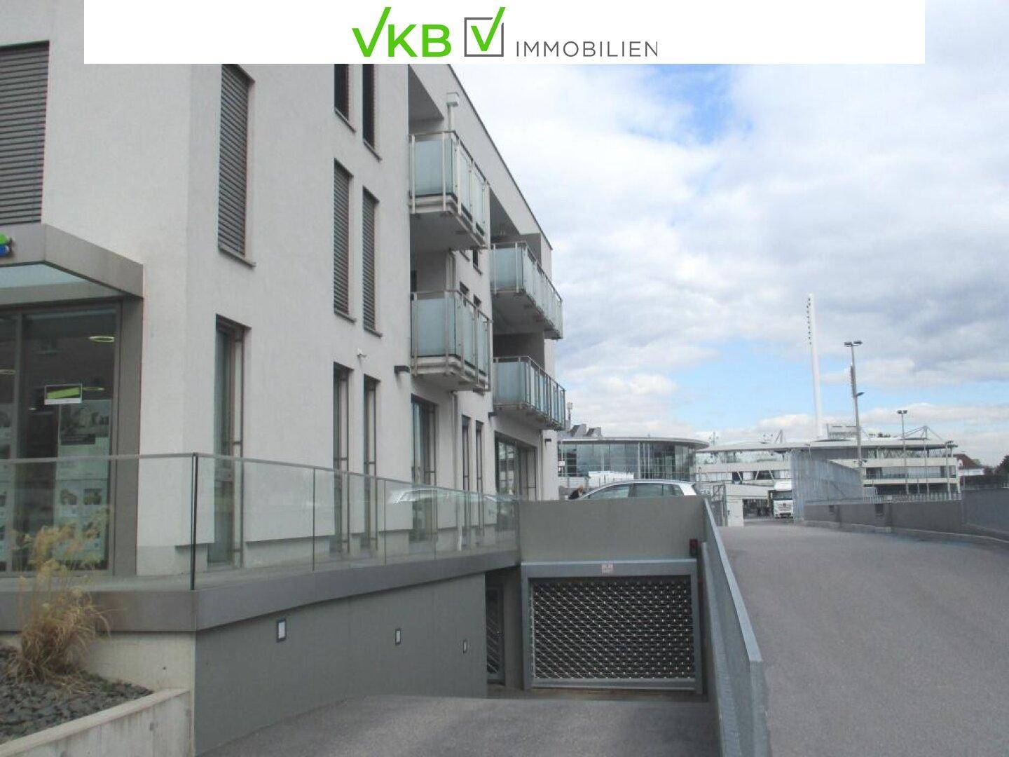 Außenansicht eines modernen Wohngebäudes mit Tiefgaragenzufahrt und Balkonen an der Fassade.