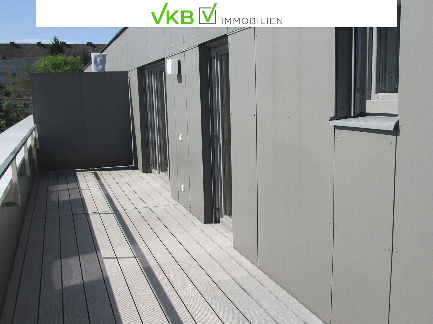 Lange Terrasse mit Dielenboden und mehreren Zugängen zu den Innenräumen des Gebäudes.