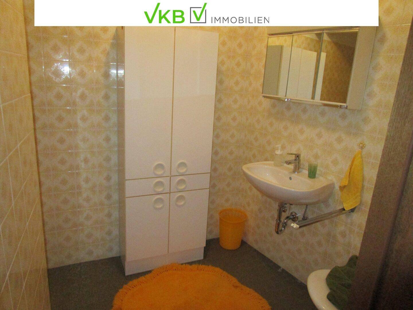 Badezimmer mit beigefarbenen Fliesen, Waschbecken und einem weißen Hochschrank.