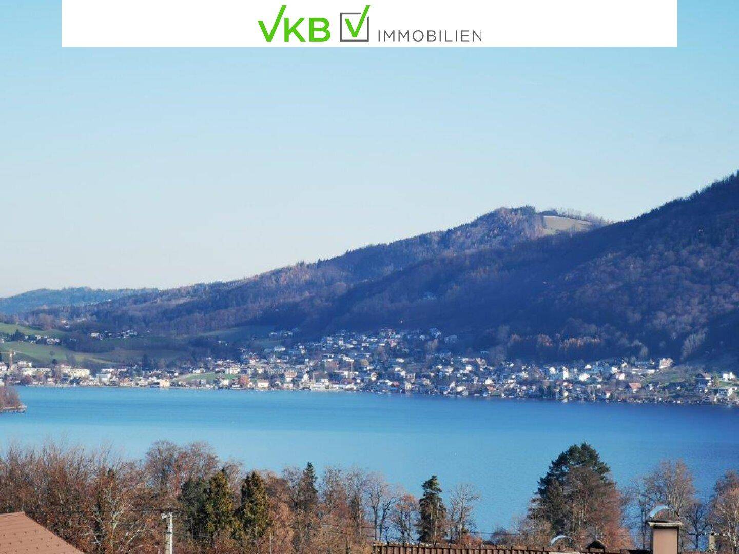 Weitläufiger Blick über einen See und die umliegende Landschaft mit bewaldeten Hügeln.