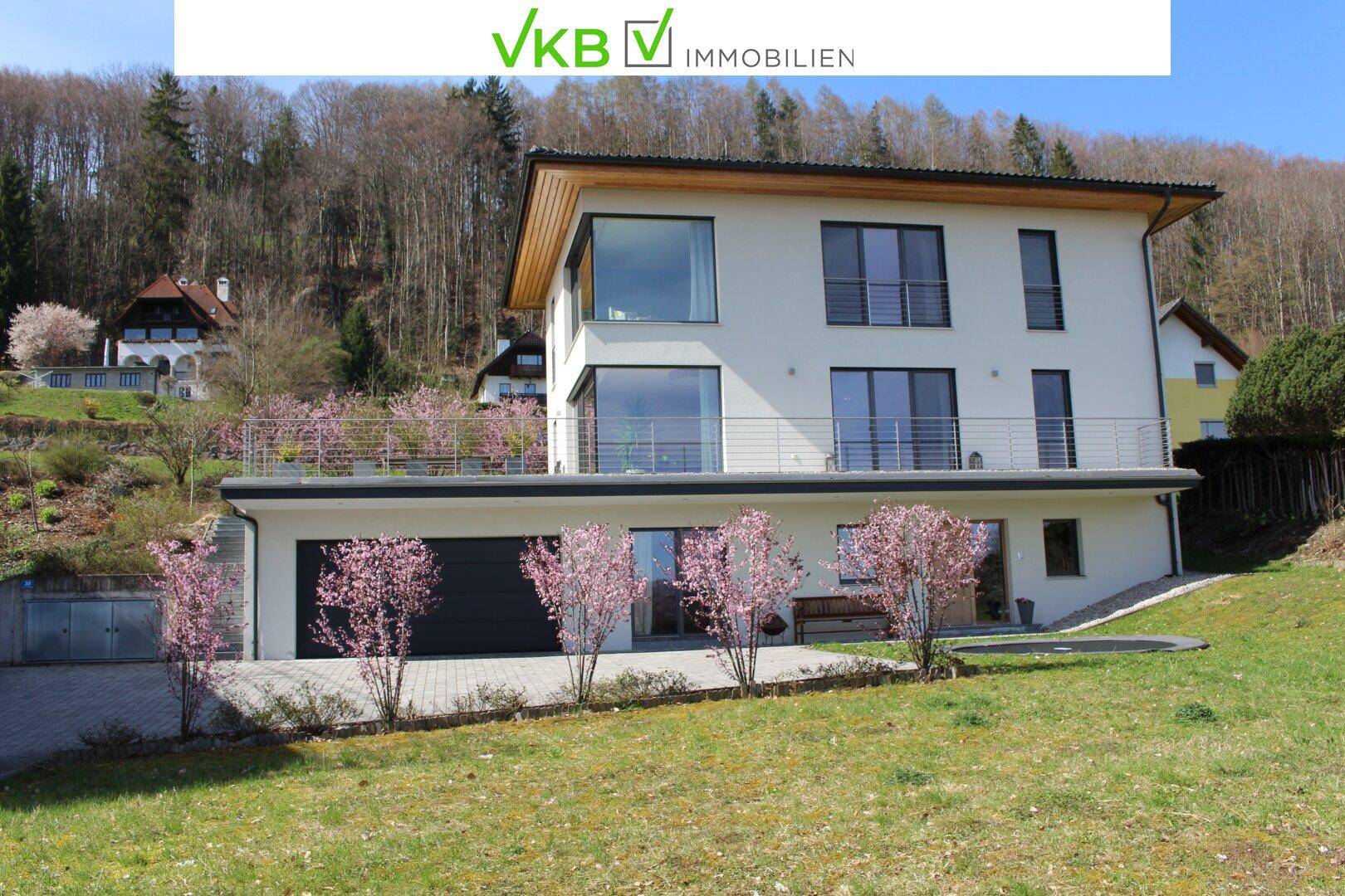 Modernes Einfamilienhaus mit weißer Fassade, großen Fenstern und mehreren Balkonen in Hanglage.
