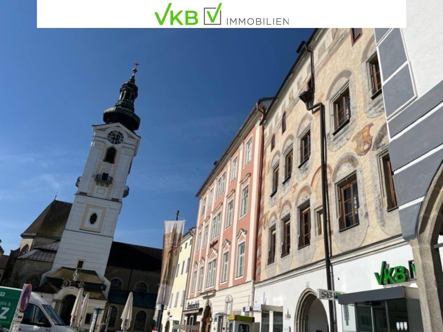 Historische Stadtansicht mit einem Kirchturm und traditionellen Gebäudefassaden unter blauem Himmel.